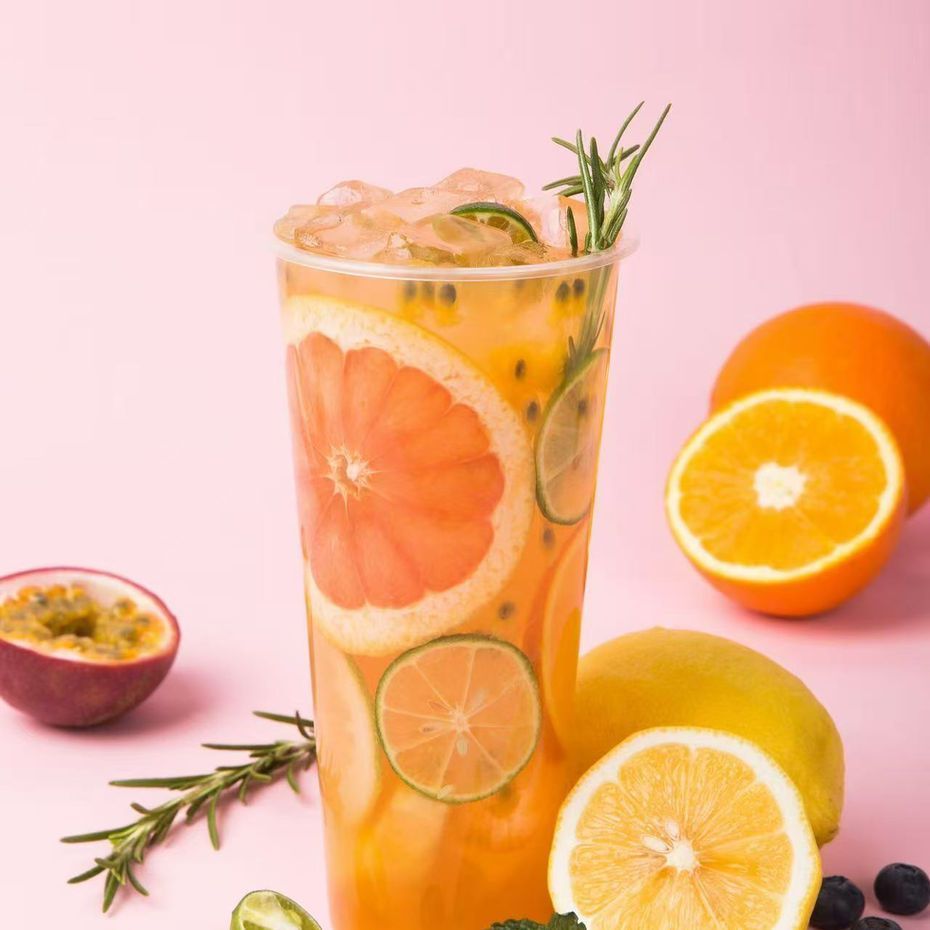 Glass of citrus fruit-infused water with grapefruit, orange, lemon, and herbs on a pink background