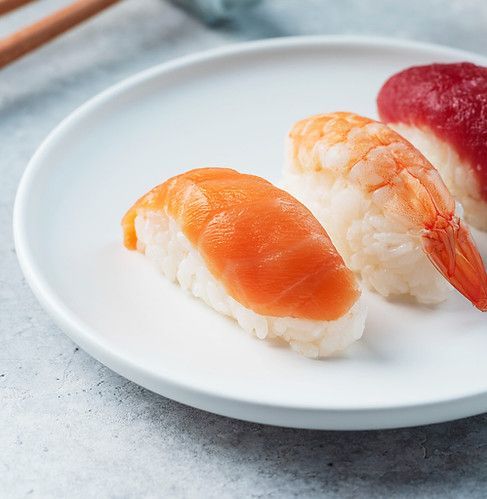Three pieces of sushi nigiri on a white plate, including salmon, shrimp, and tuna.