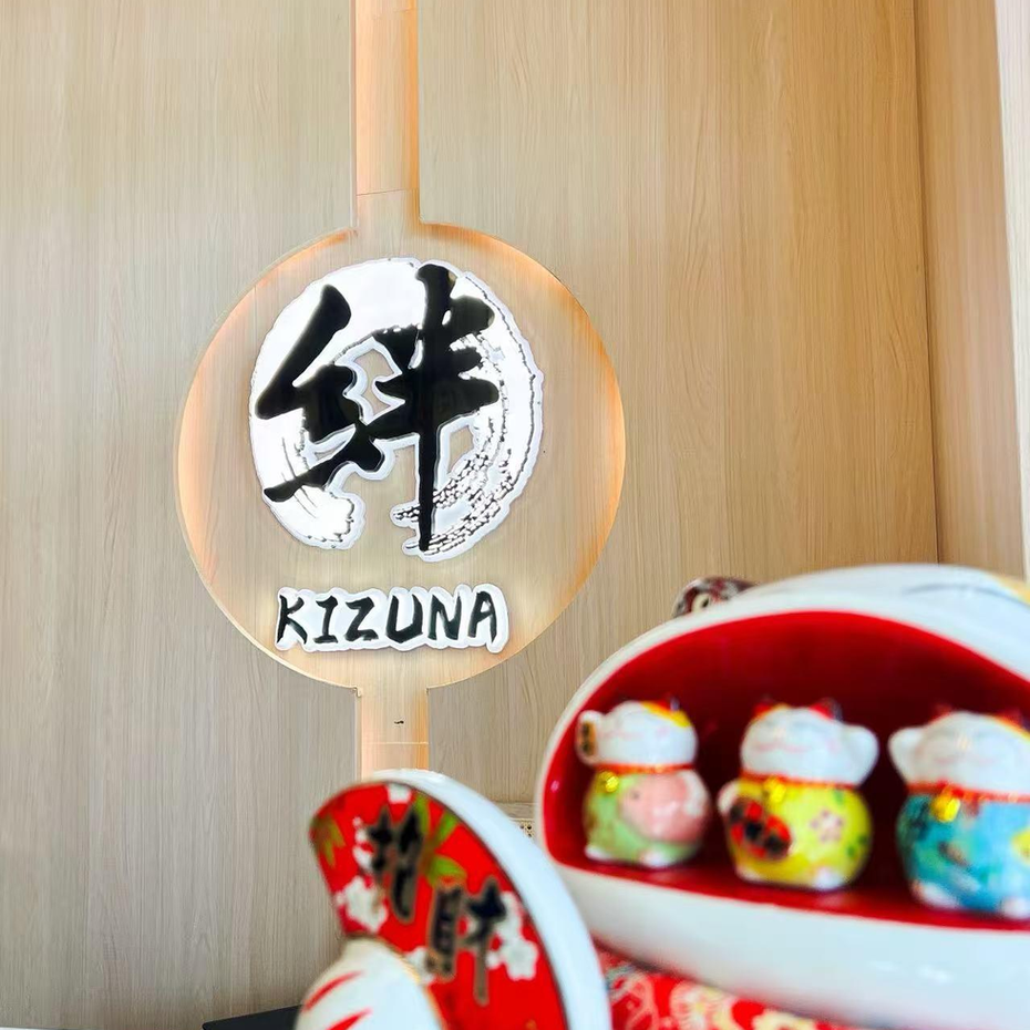 Wooden KIZUNA sign with Japanese calligraphy beside a red tray of small figurines