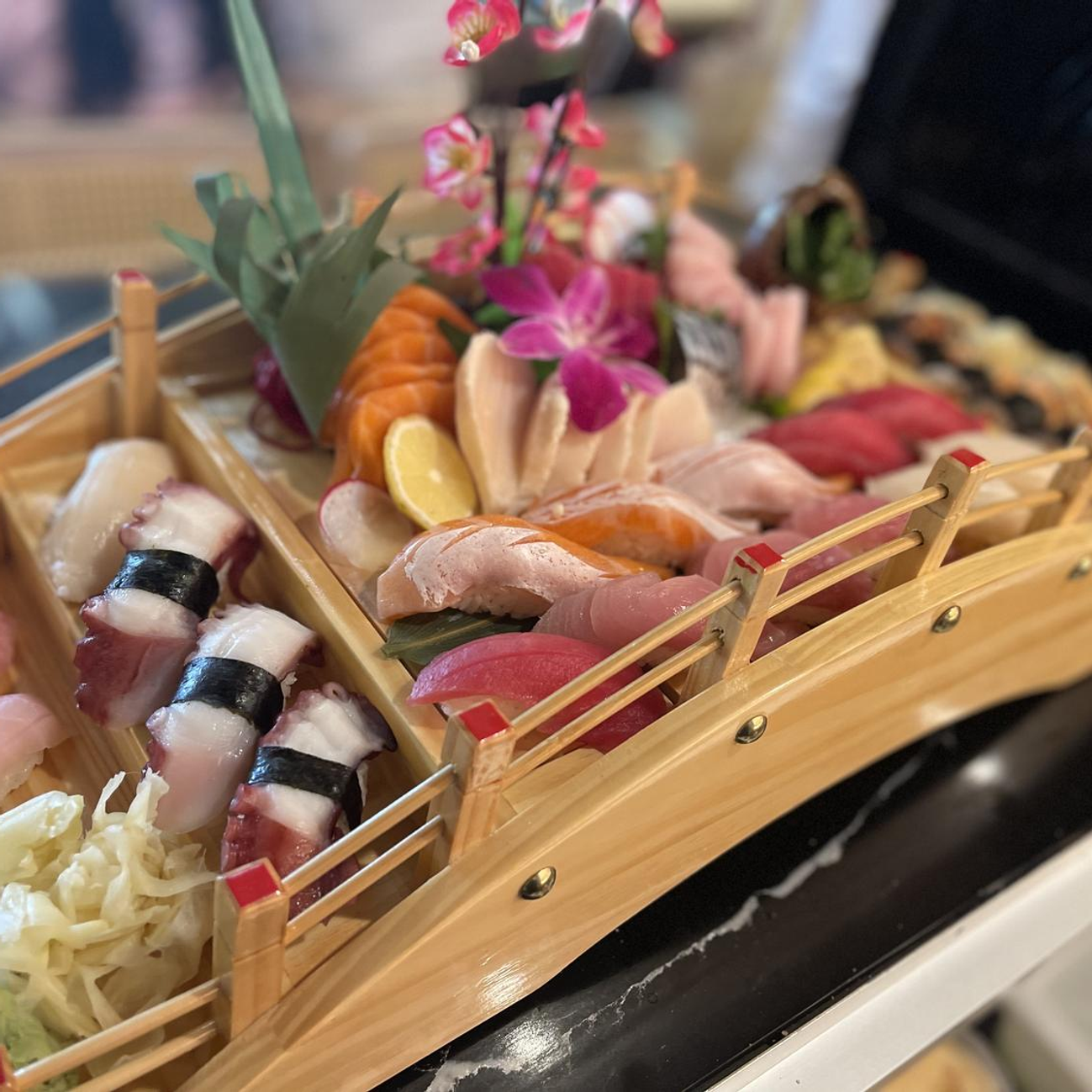 Sushi platter in a wooden boat tray with assorted nigiri, sashimi, and flowers