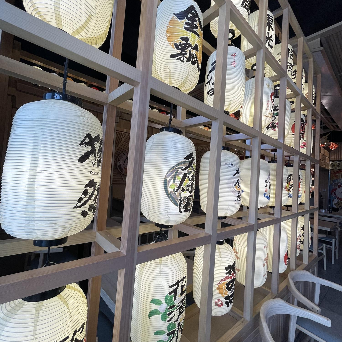 Rows of glowing white paper lanterns with black Japanese calligraphy in a wooden display rack