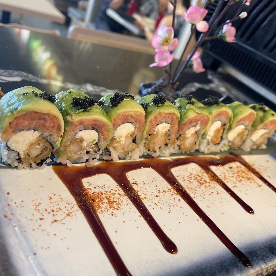 Sushi rolls lined on a plate with dark sauce drizzles, topped with green garnish and a pink flower garnish