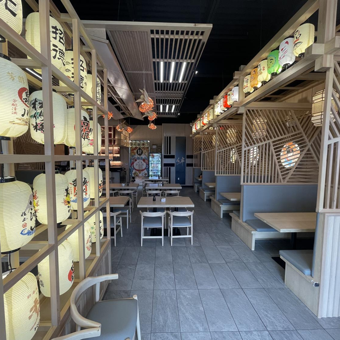 Narrow Japanese-style dining aisle with lanterns, tables, booths, and wooden shelves lining both sides