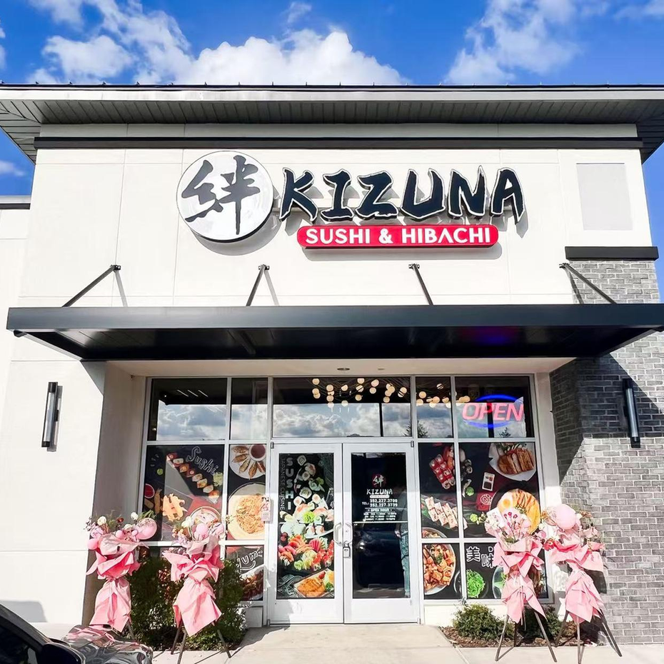 Kizuna Sushi & Hibachi storefront with pink flower grand opening displays under a bright sky