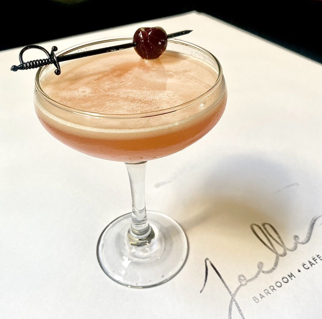 A martini with a cherry on a toothpick sits on a table