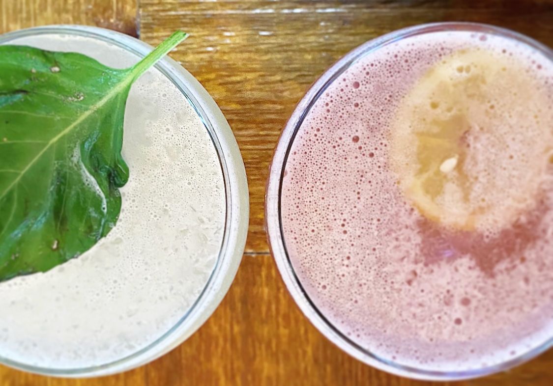 Two glasses of different colored liquids are sitting on a wooden table.