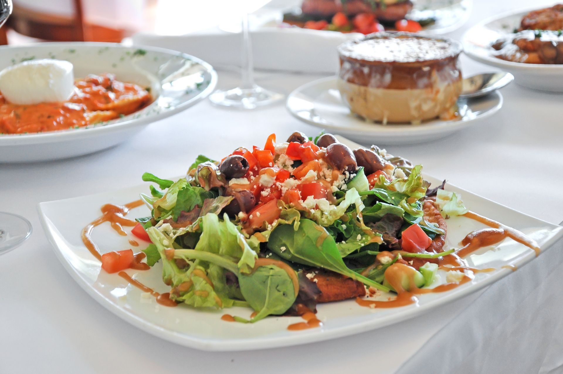 A salad on a white plate on a table with other plates of food.