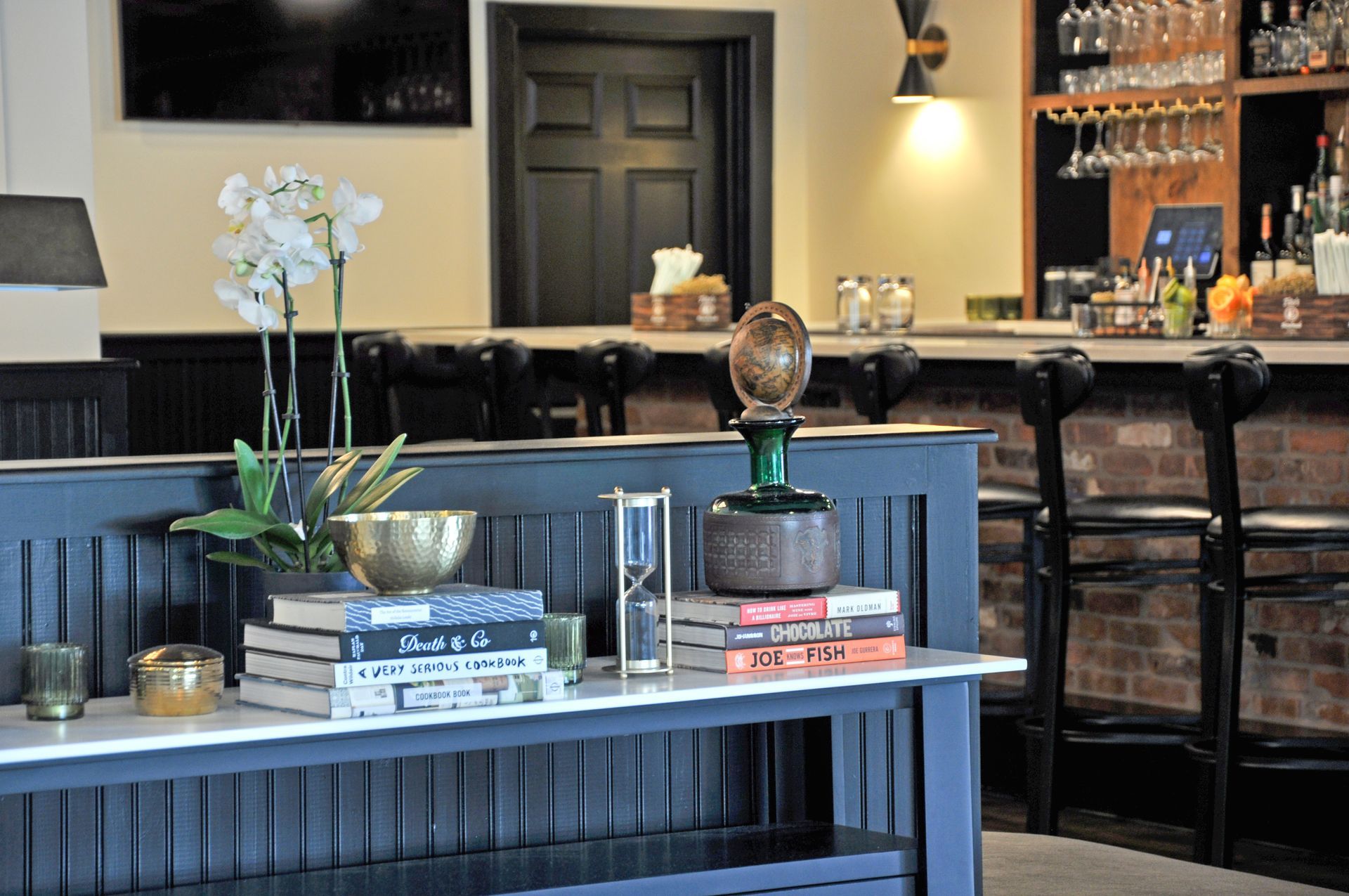 A table with a vase of flowers and books on it in front of a bar.