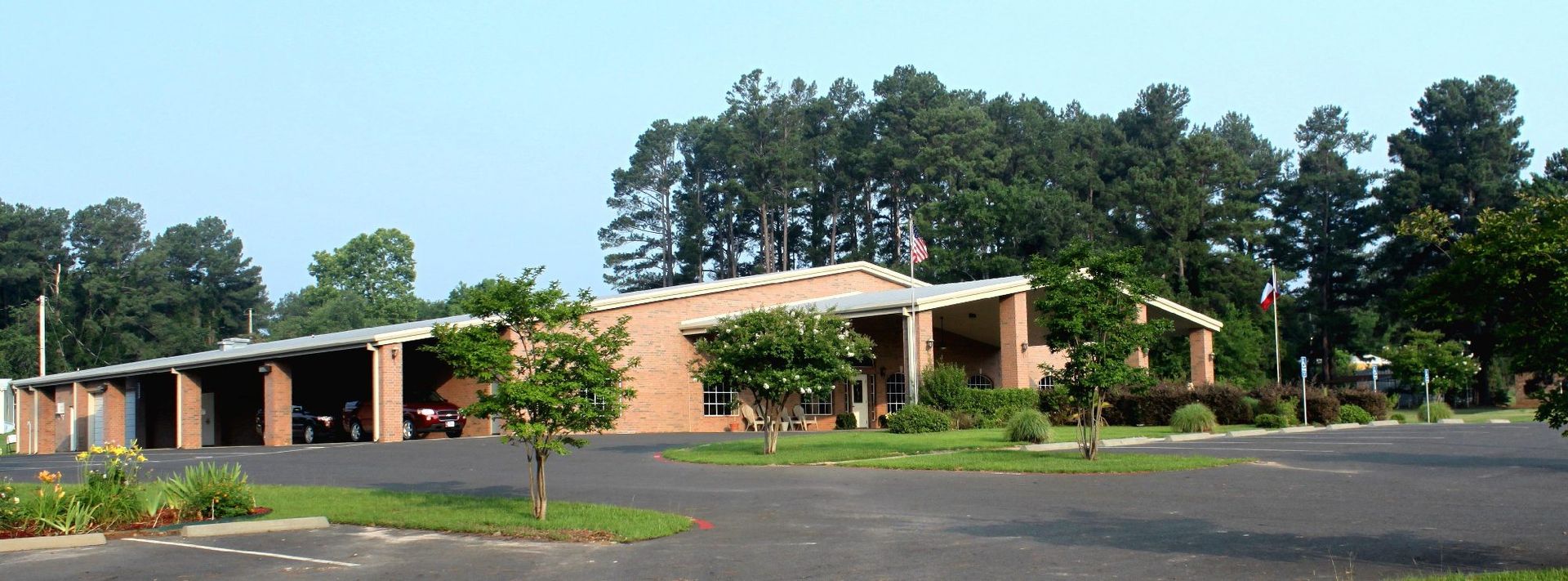 Low-slung brick building with a covered walkway and several trees in front.