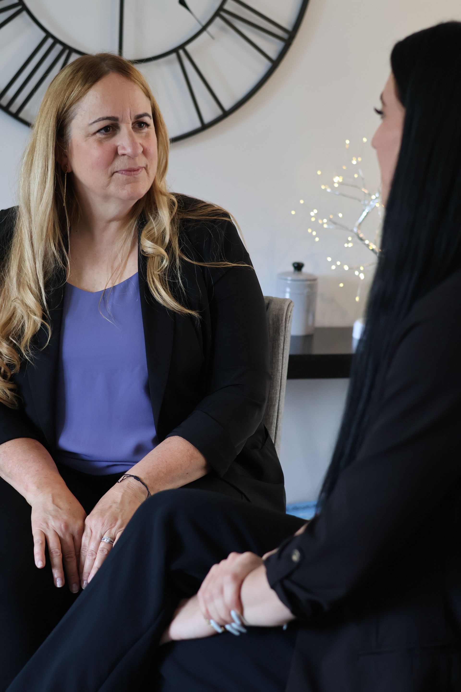 two women are sitting next to each other and talking in front of a clock .