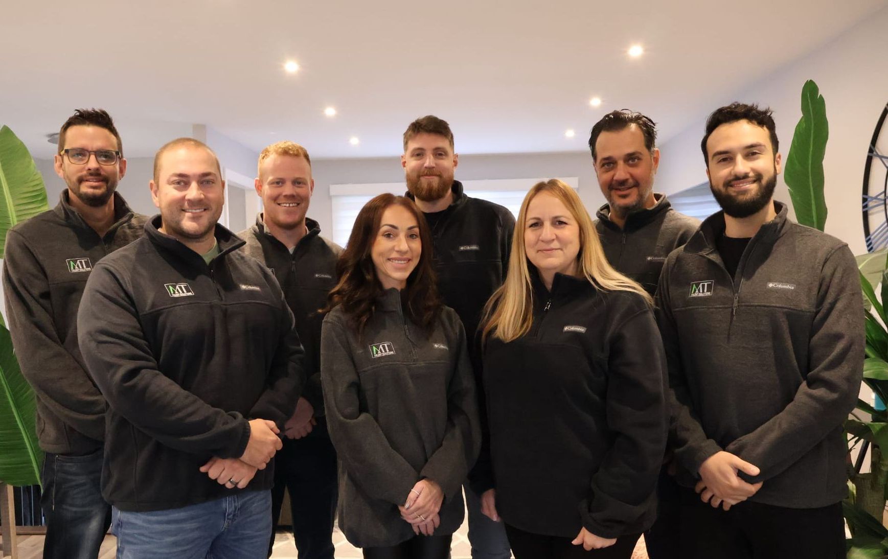 Seven people in black jackets standing together indoors, smiling at the camera.