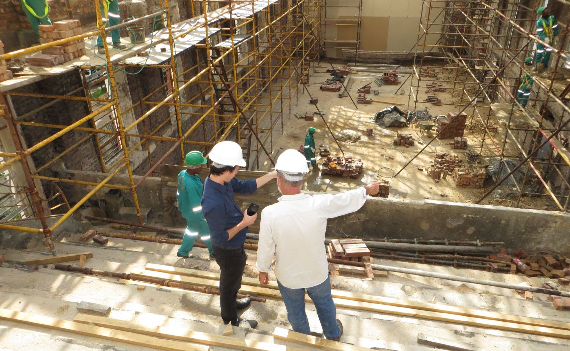 Construction workers in hard hats overlooking a scaffolded excavation site with debris below