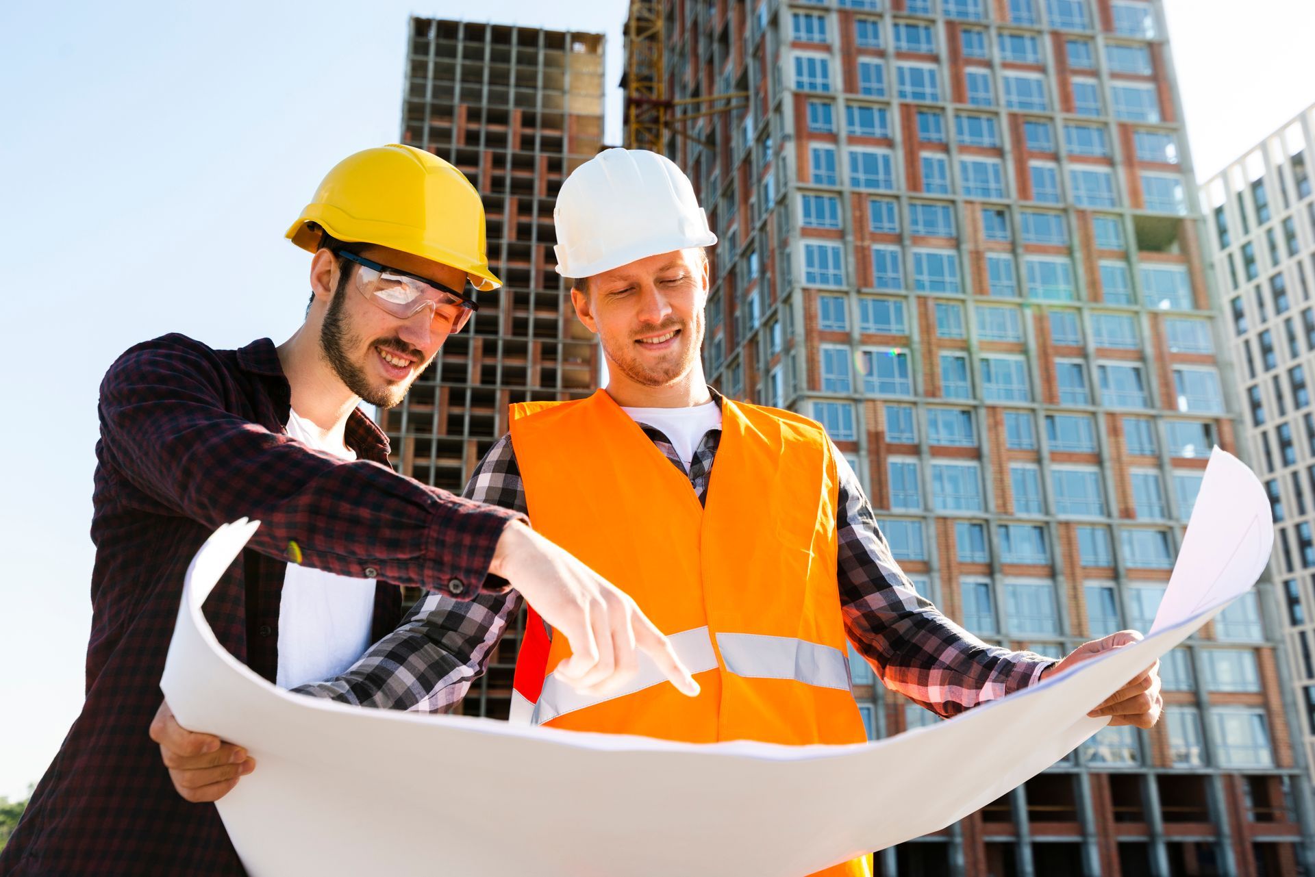 Two construction workers in hard hats reviewing blueprints at a building site
