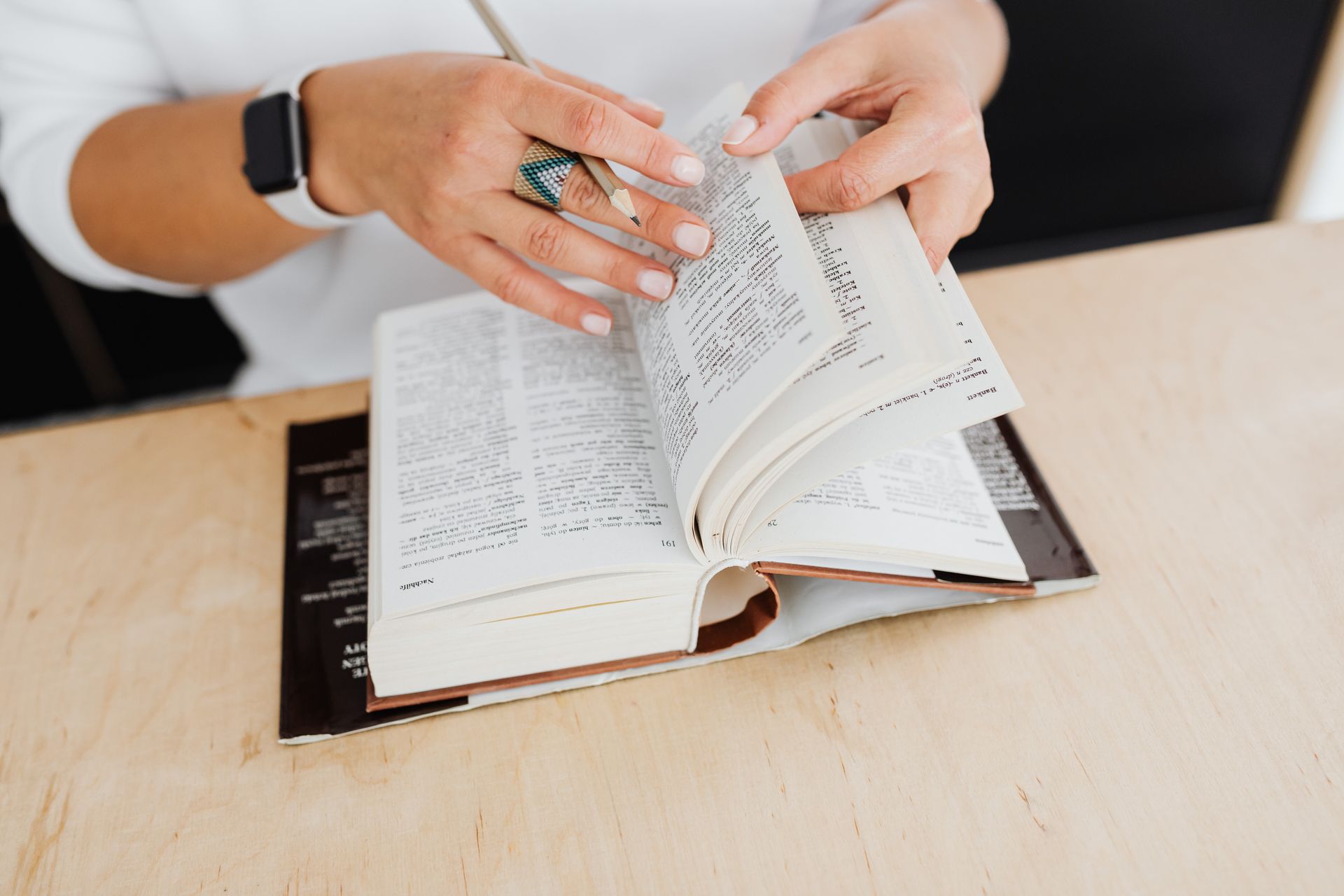 Hands turning pages of an open book on a light wooden table