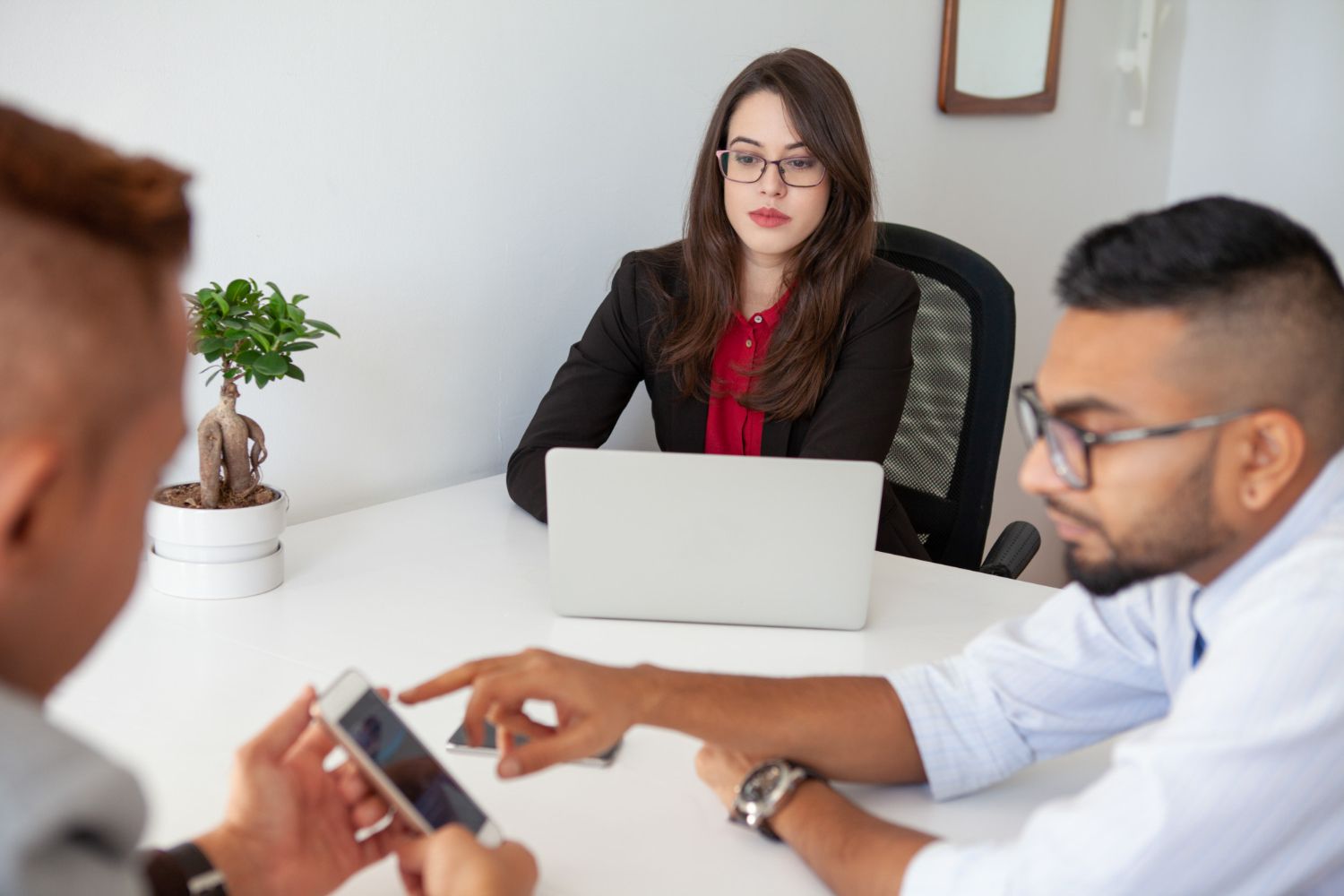 Business meeting with three people around a laptop, one woman speaking while others review a phone and document