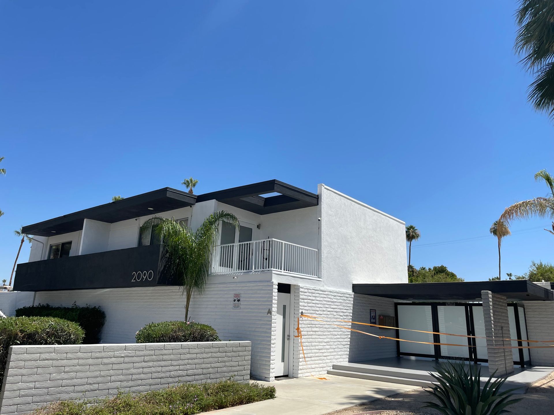 White two-story building with black trim against a bright blue sky; palm tree visible.