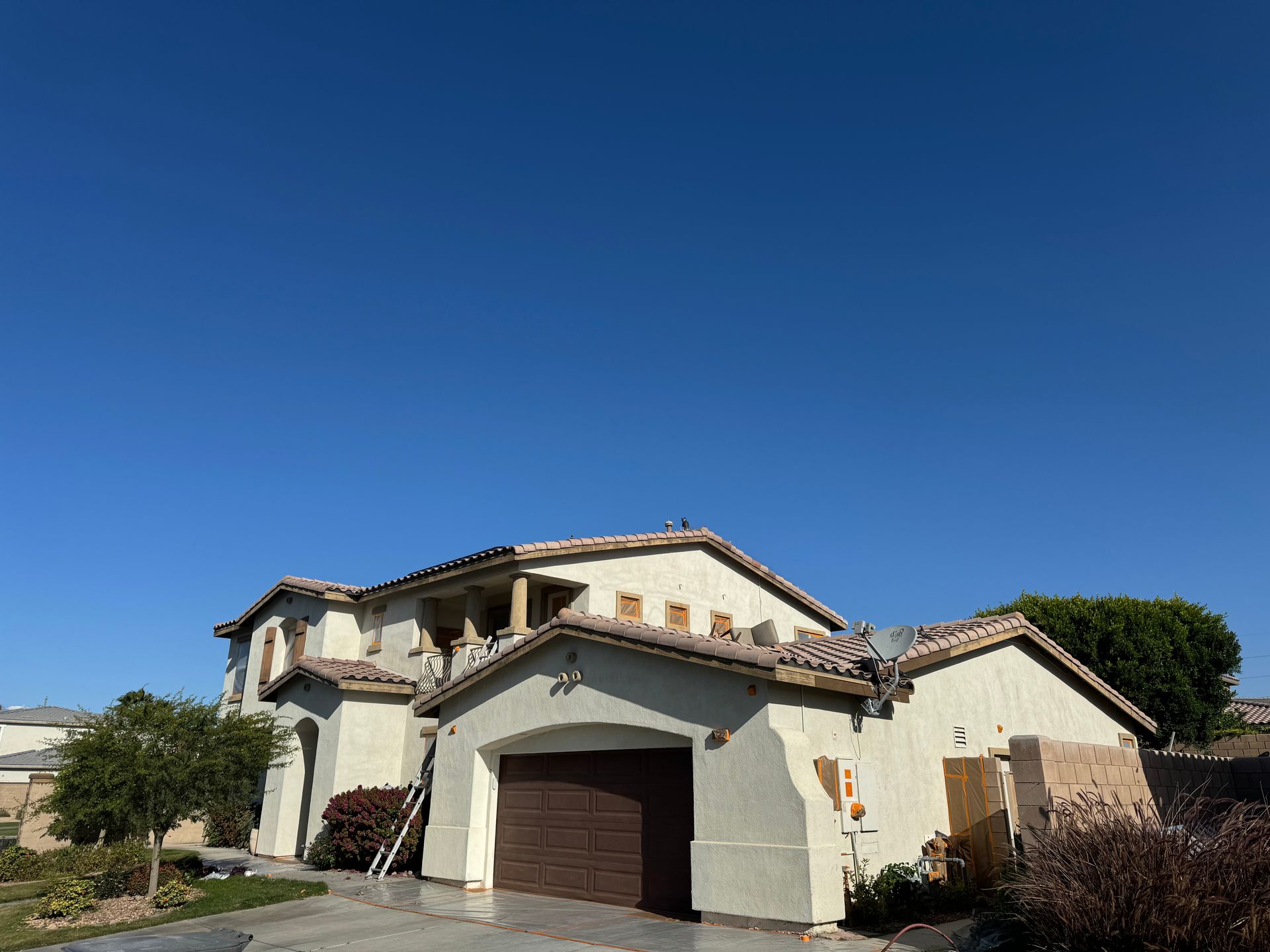 Two-story beige house with brown garage door under a clear blue sky.