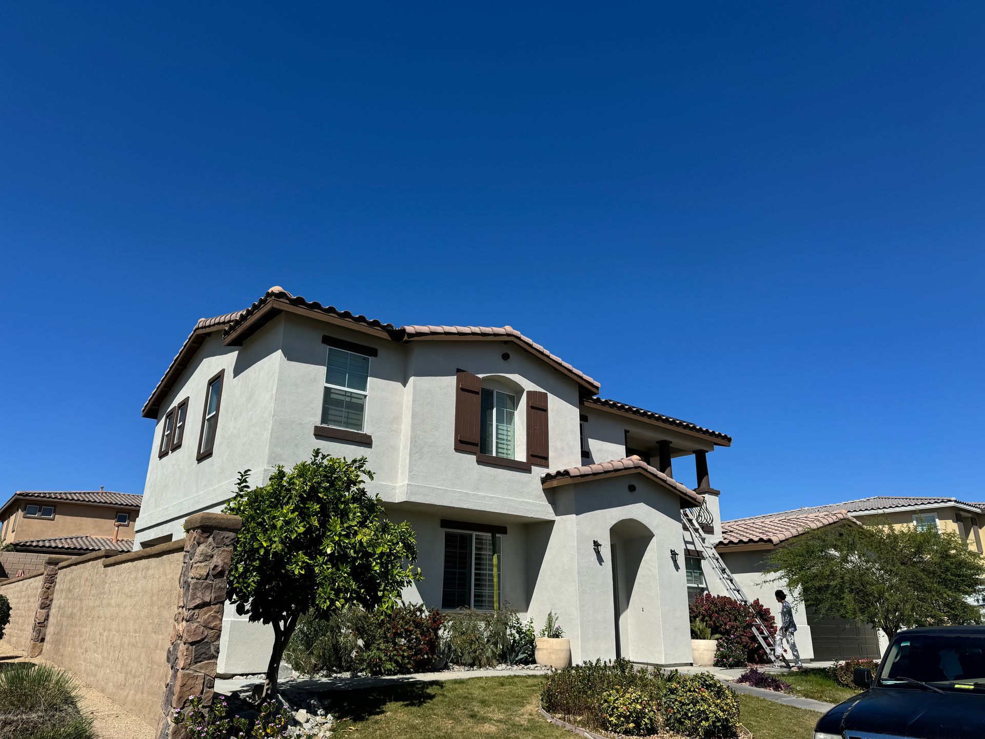 Two-story beige house with brown shutters under a clear blue sky.