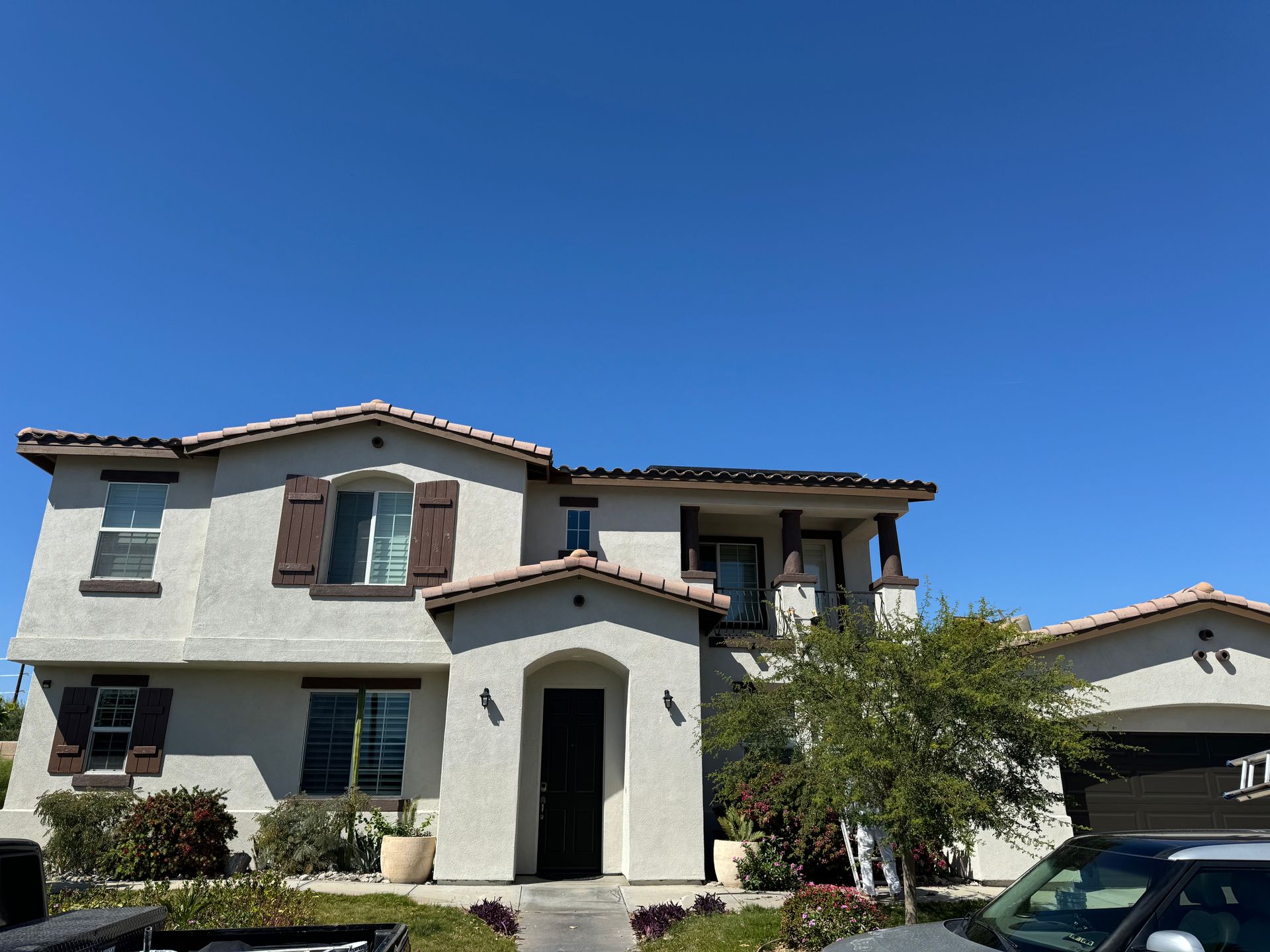 Two-story stucco house with brown shutters under a clear blue sky.