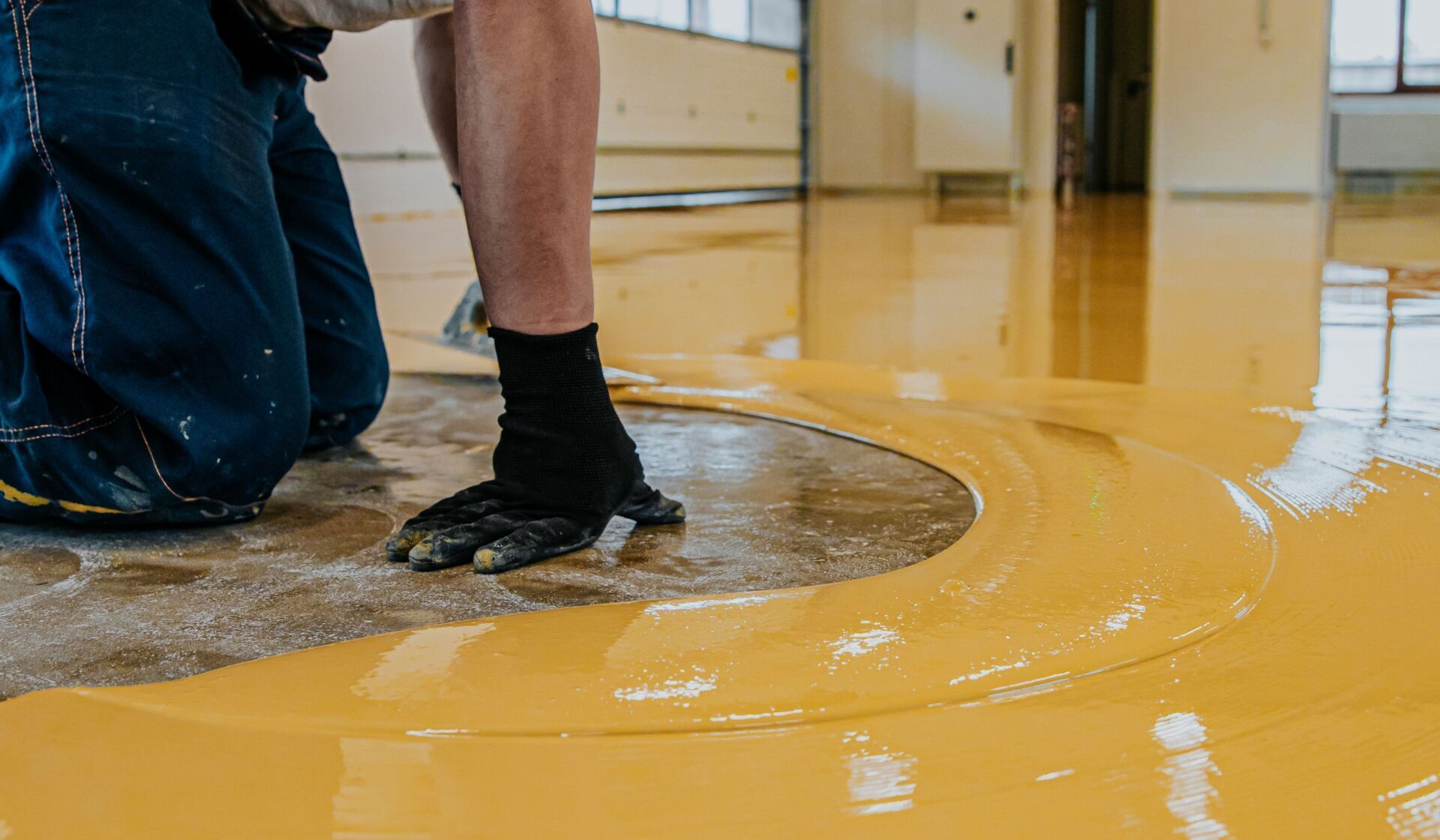 Person applying yellow epoxy floor coating indoors.