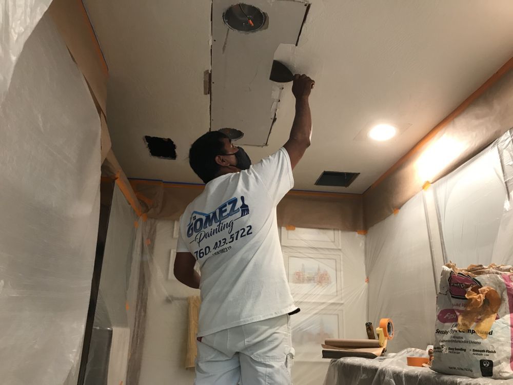 Person patching a ceiling with a trowel; room covered in plastic sheeting.