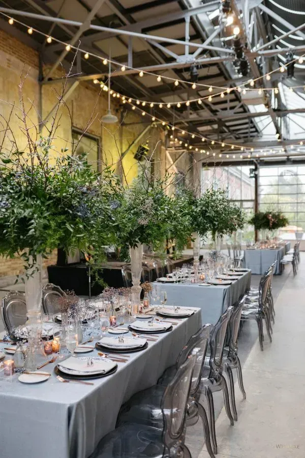 A long table set for a wedding reception in a large room with lots of tables and chairs.