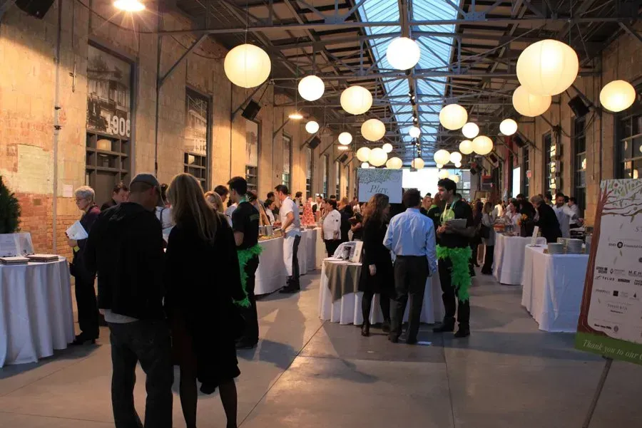 A group of people are standing in a room with tables and lanterns hanging from the ceiling.