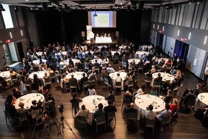 A large group of people are sitting at tables in a large auditorium.