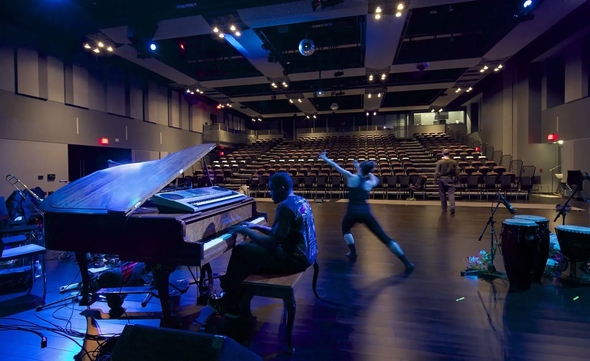 A man is playing a piano while a woman is dancing on a stage.