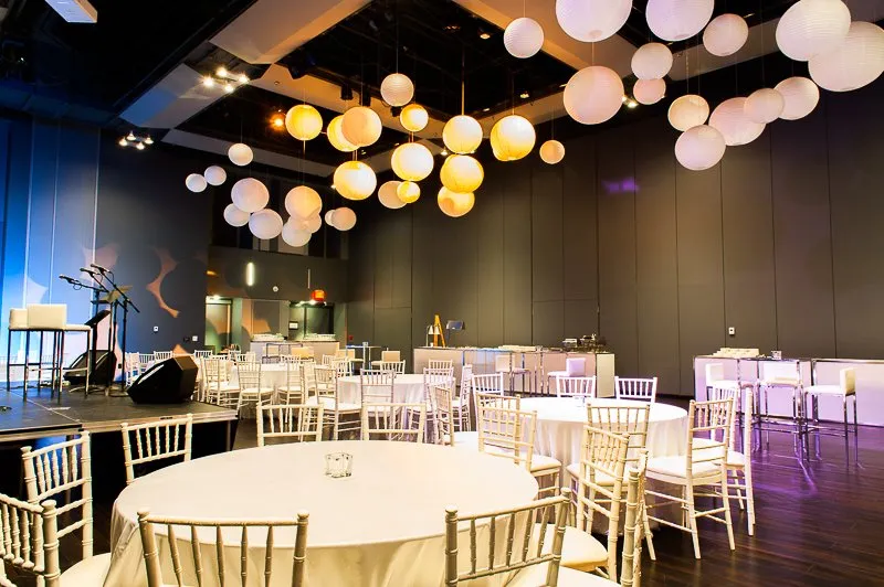 A large room with tables and chairs and lanterns hanging from the ceiling.