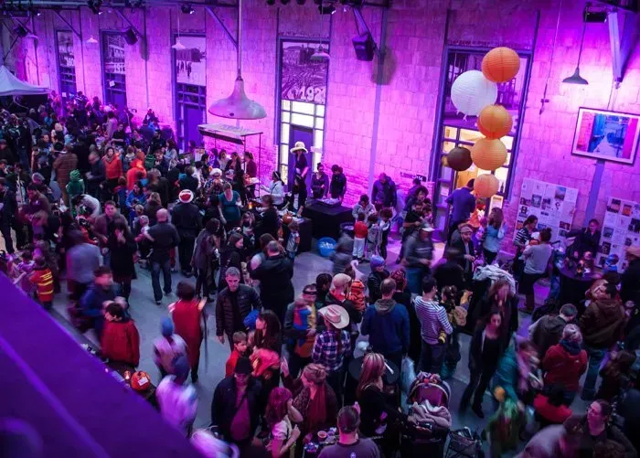 A large crowd of people are gathered in a room with purple lights.