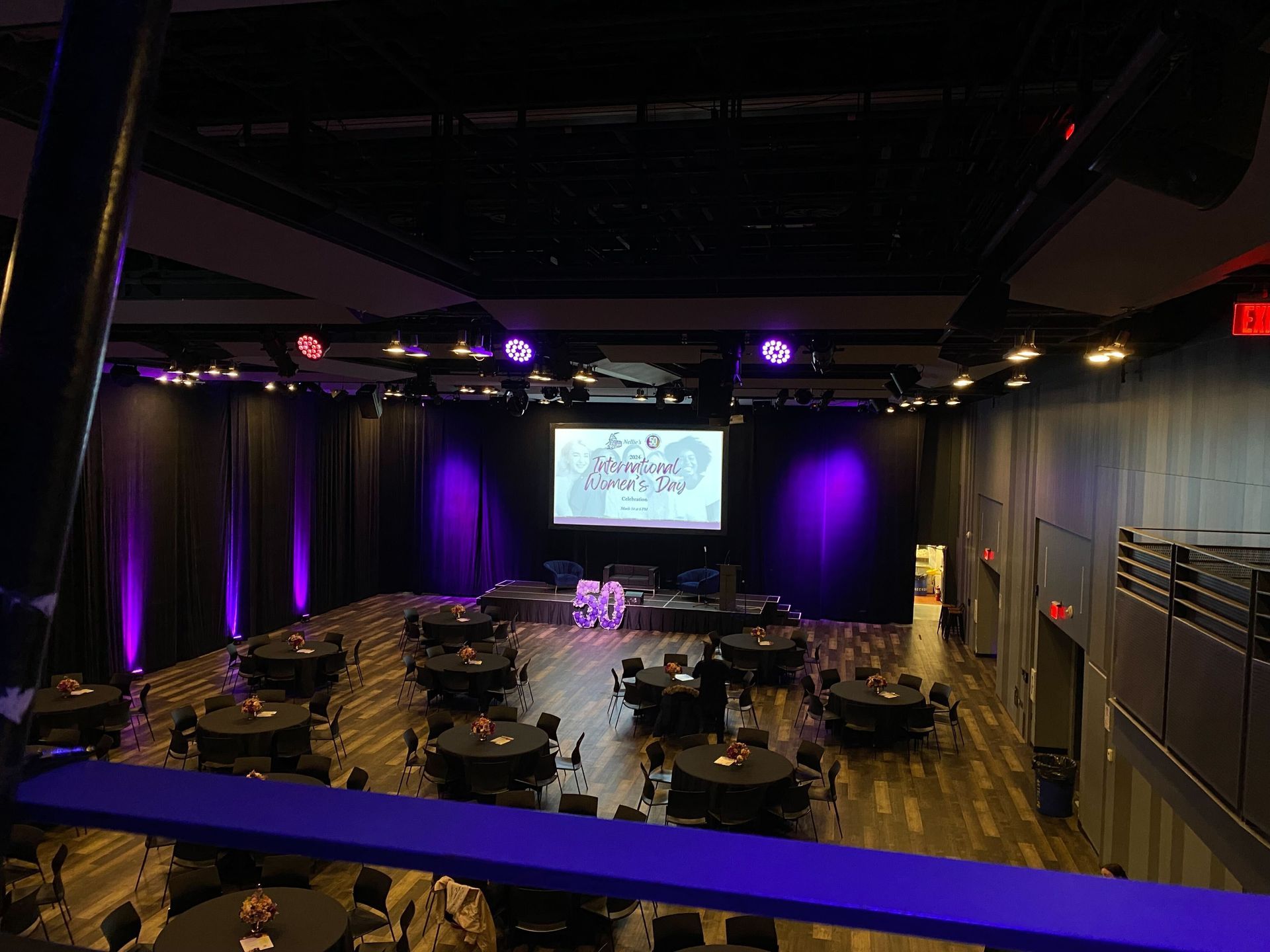 A large room with tables and chairs and a large screen on the stage.
