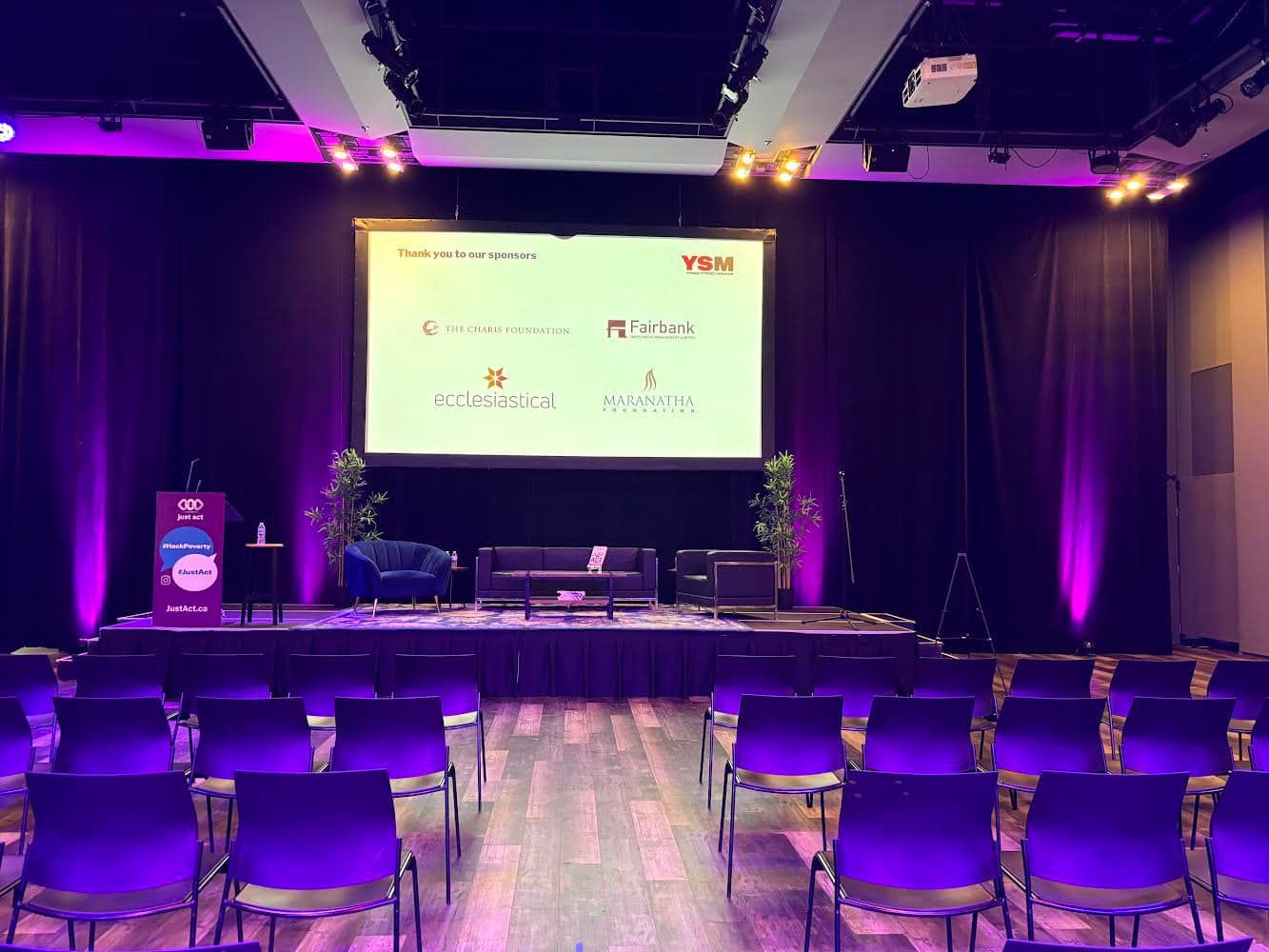 A conference room with purple chairs and a large screen.