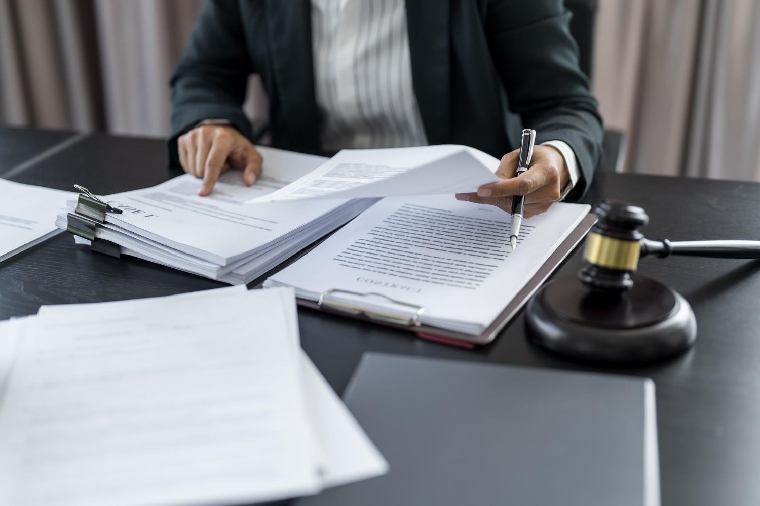 Person reviewing legal documents at a desk with a gavel and notebook, signing papers.