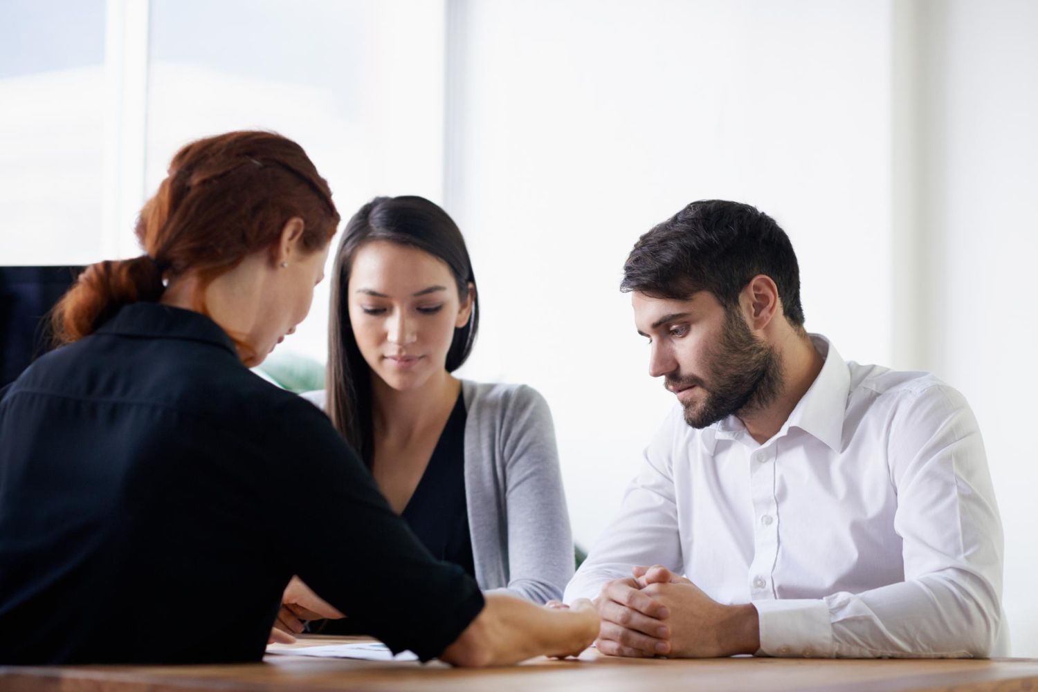 Three people in a meeting, leaning over papers at a table in a bright office