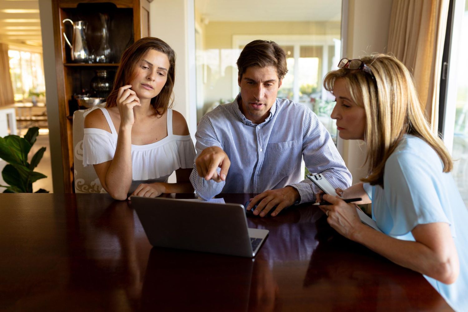 Three people discussing a laptop at a dining table in a living room