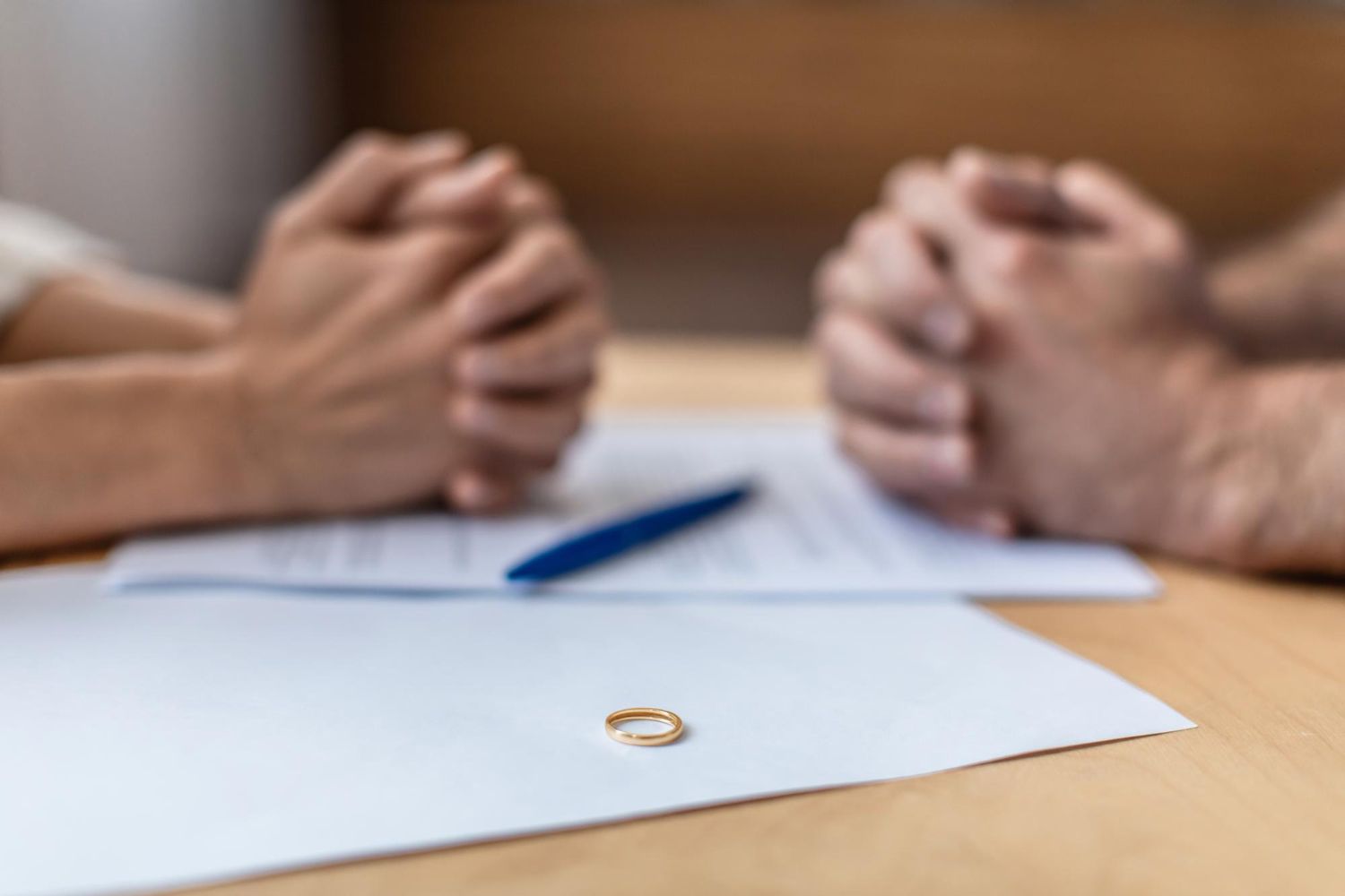 Two people clasping hands across a table with a pen and papers, suggesting a negotiation or agreement.