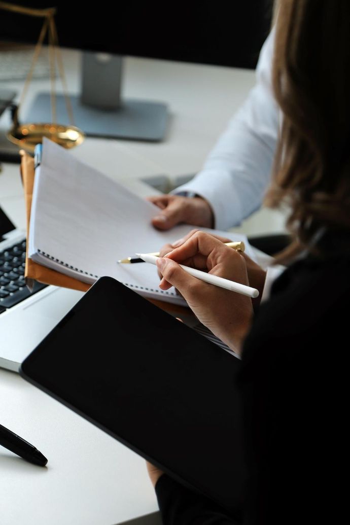 Person writing notes in a notebook at a desk with a tablet nearby