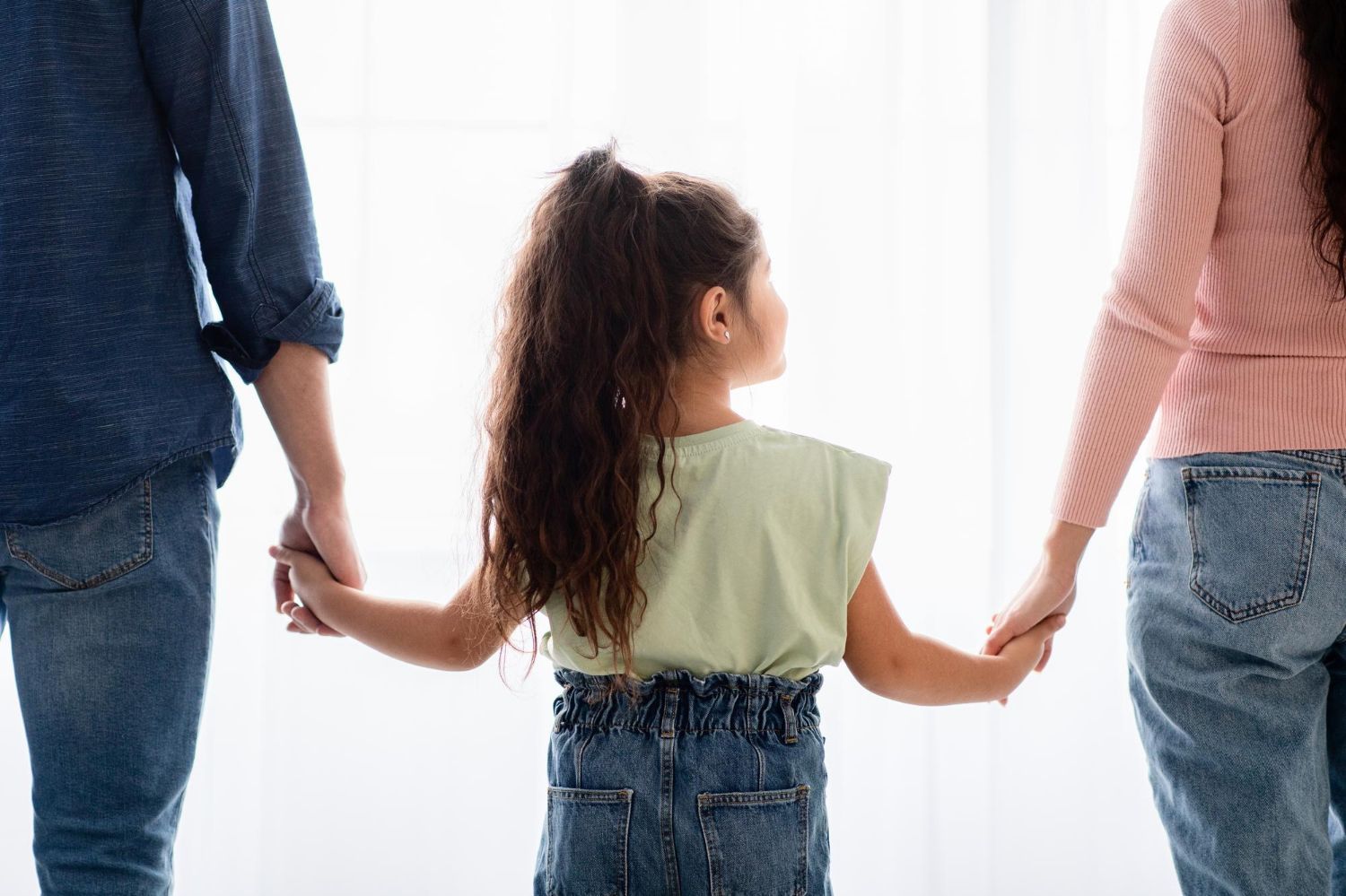 Three people holding hands, seen from behind against a bright white background.