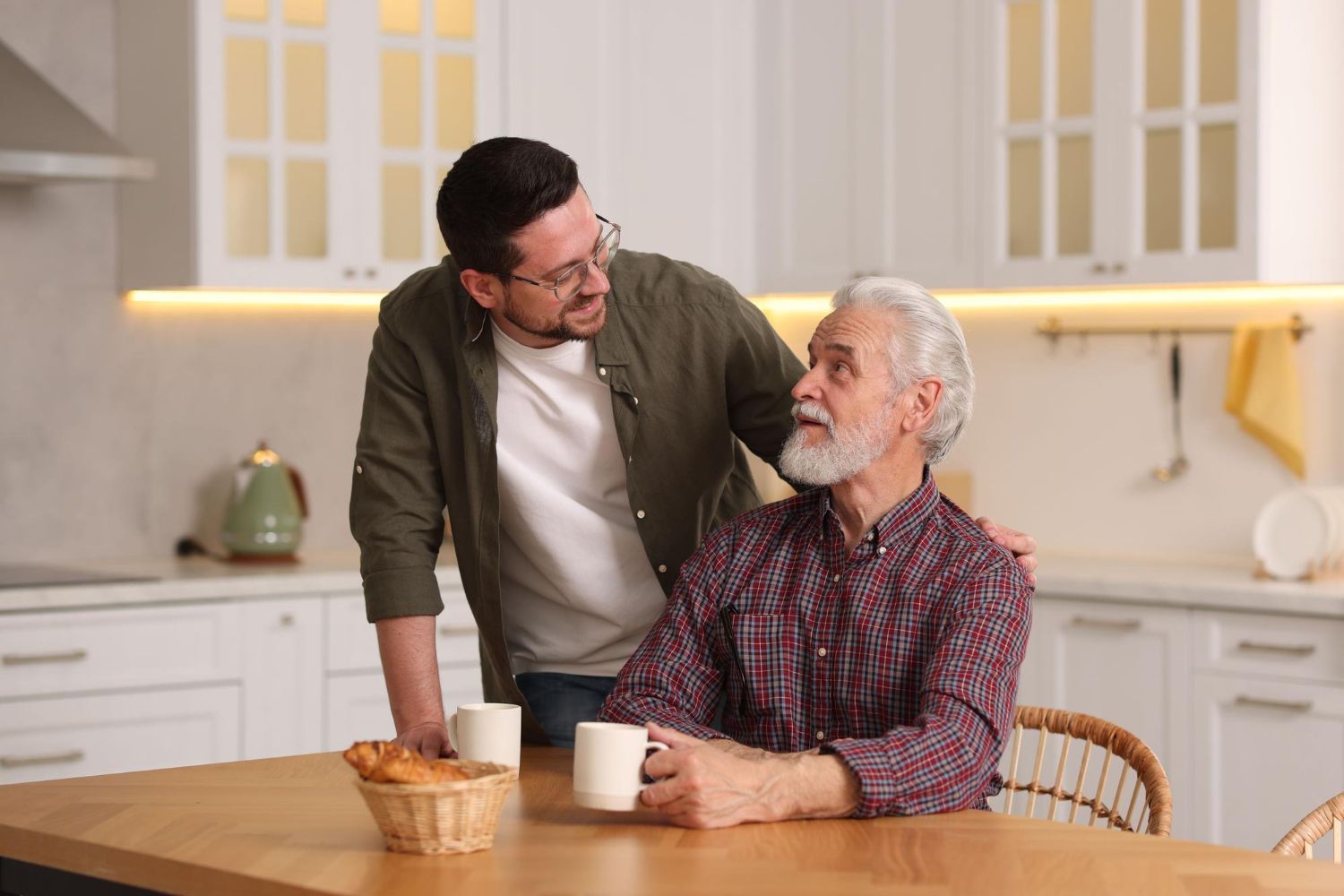 Two men chatting in a bright kitchen beside a table with a basket and mug