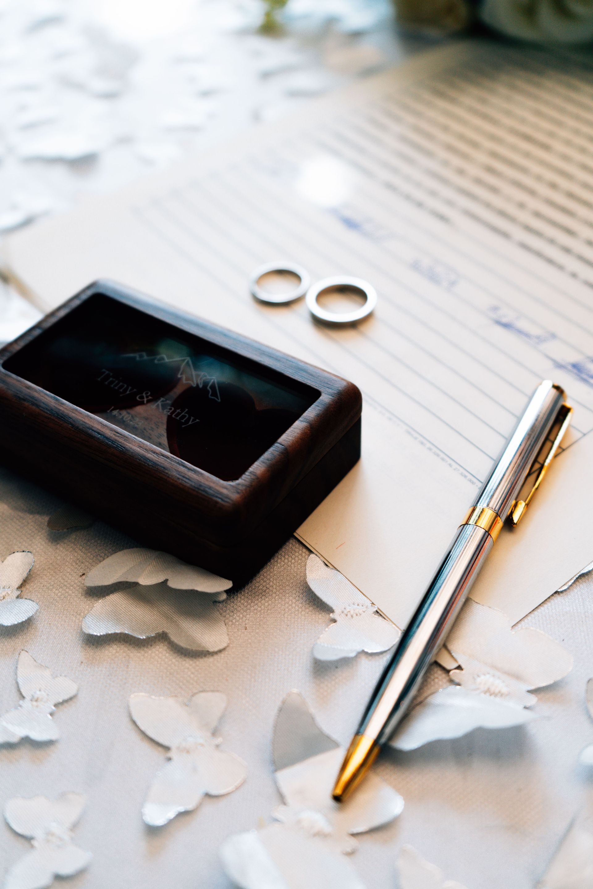 Wedding rings and a silver pen on a lined paper with scattered white petals