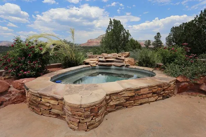 Stone hot tub in a desert garden with red rocks and shrubs.