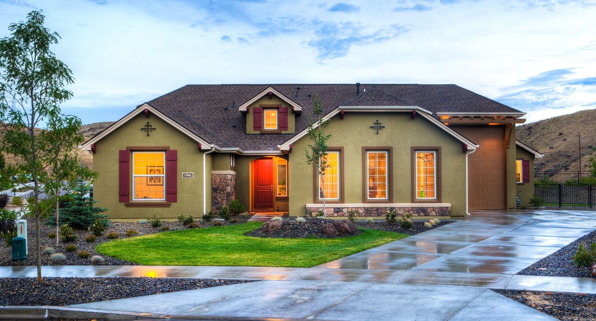 Modern house with warm exterior lights and a wet driveway