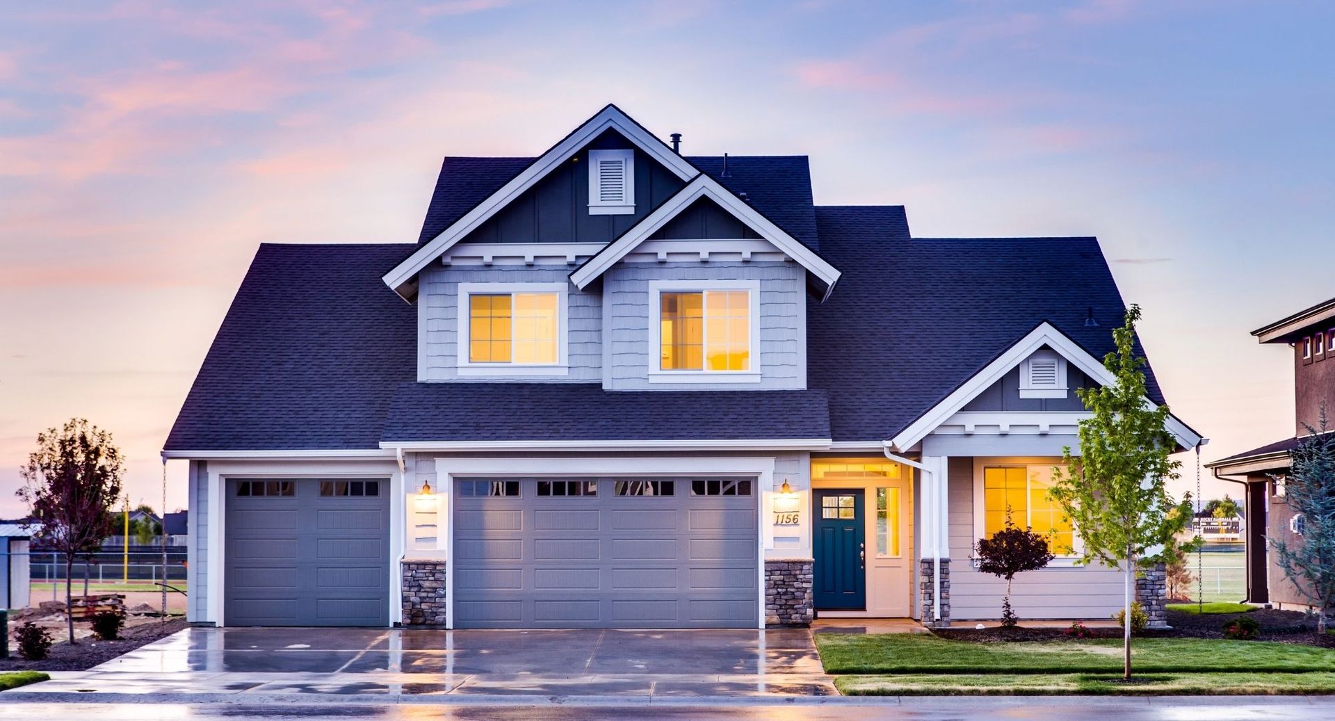 Modern gray suburban house with lit windows and a two-car garage