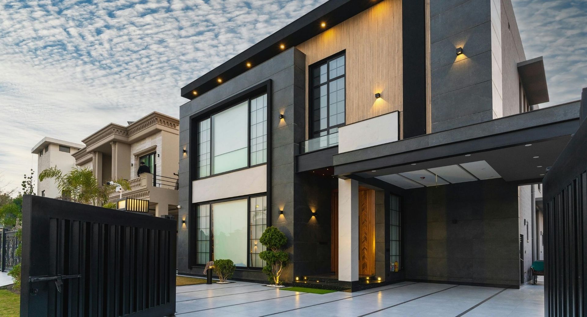 Modern two-story house exterior with large windows, gray facade, and driveway at dusk