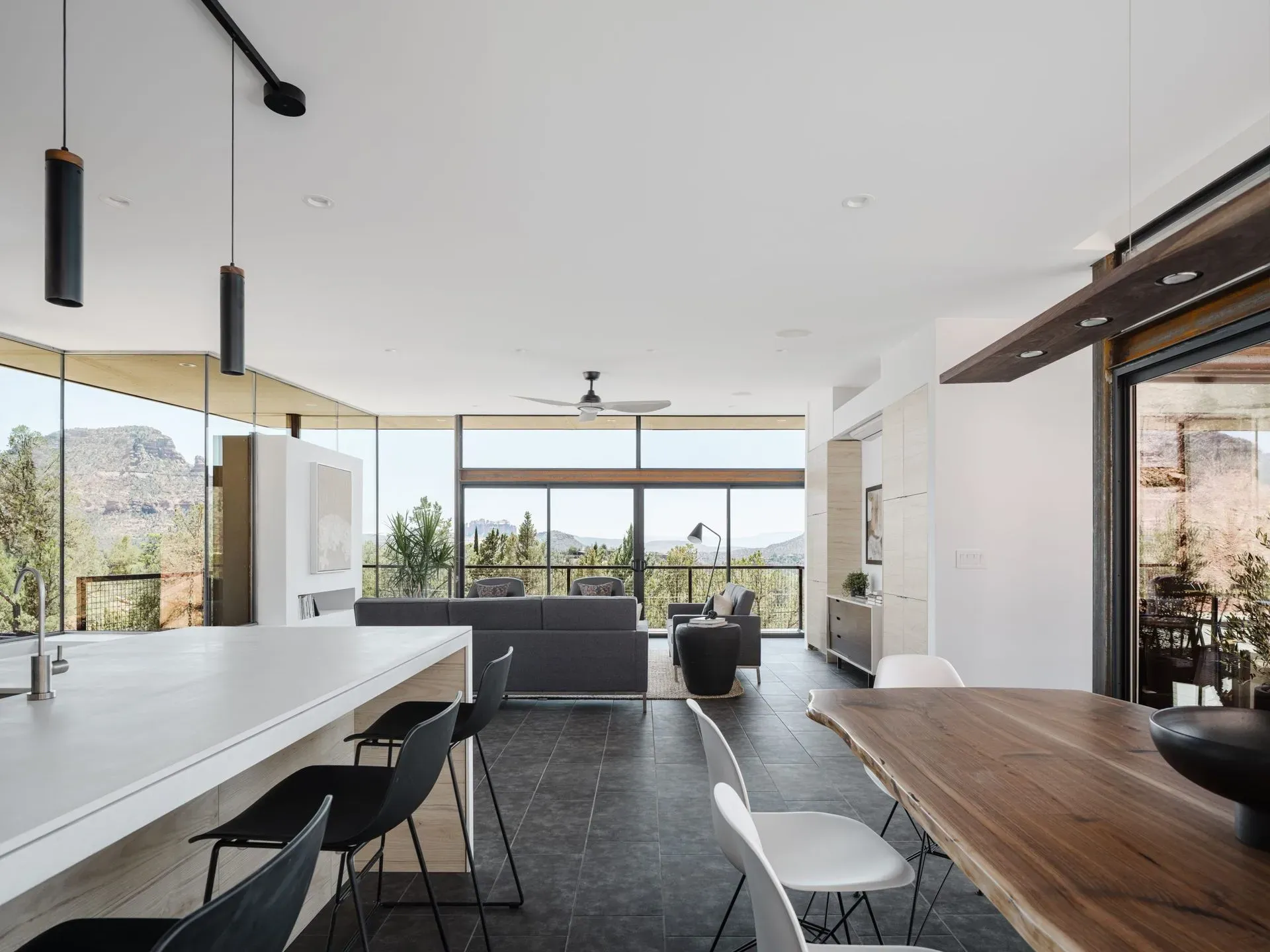 Modern open-plan kitchen and dining room with white island, wood table, black chairs, and large windows