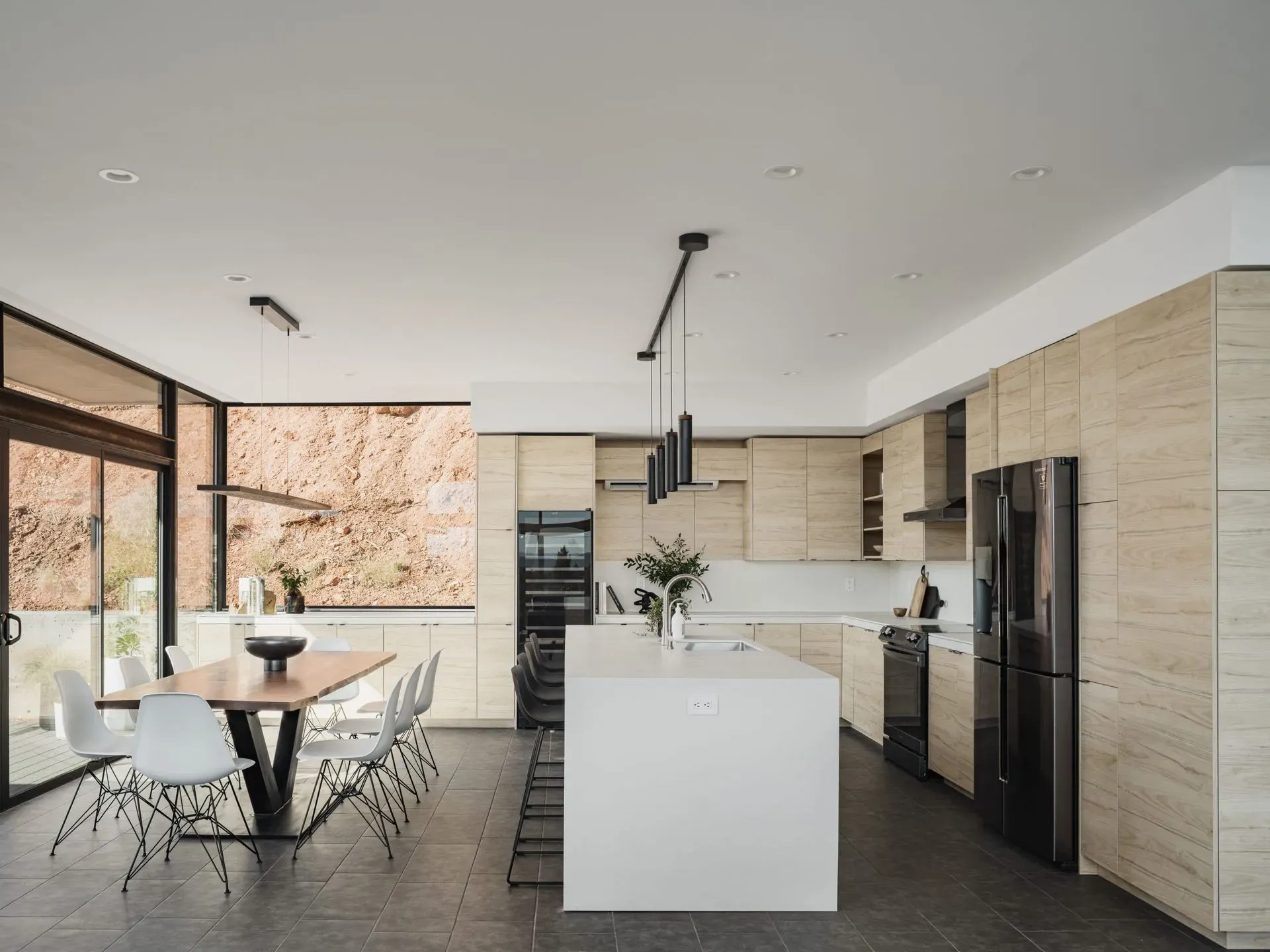Modern open-plan kitchen and dining area with white island, black appliances, and floor-to-ceiling windows