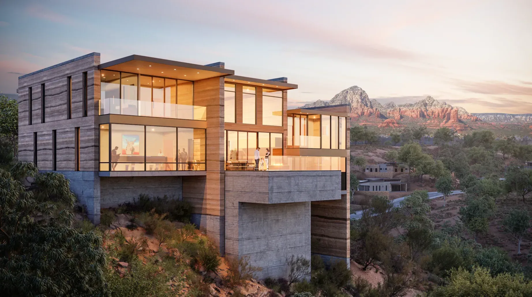 Modern hillside house with large glass windows at sunset, overlooking a rocky desert landscape