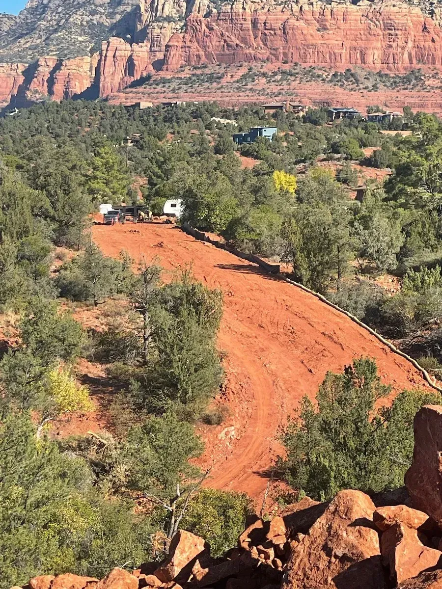 Red dirt road winding through green trees toward red sandstone cliffs under a clear sky