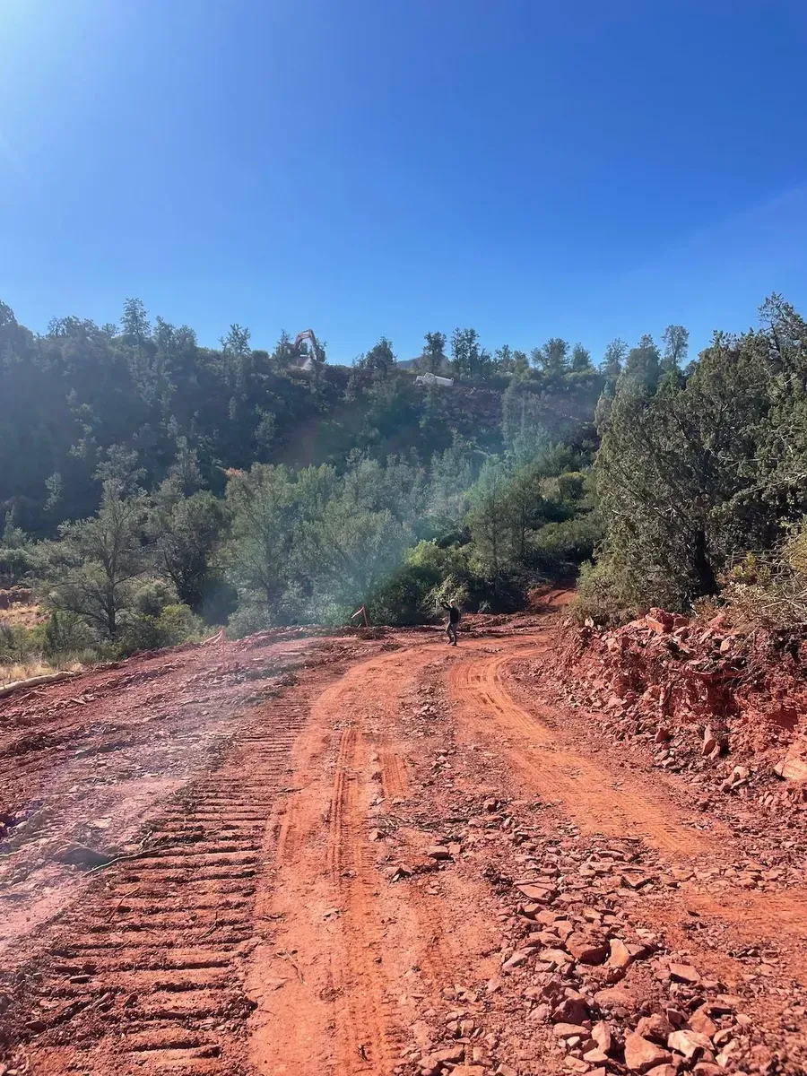 Red dirt road curving through a wooded hillside under a bright blue sky